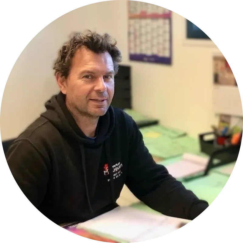 Ouvrier couvreur travaillant sur une toiture en tuiles rouges, portant casque de protection bleu et harnais de sécurité