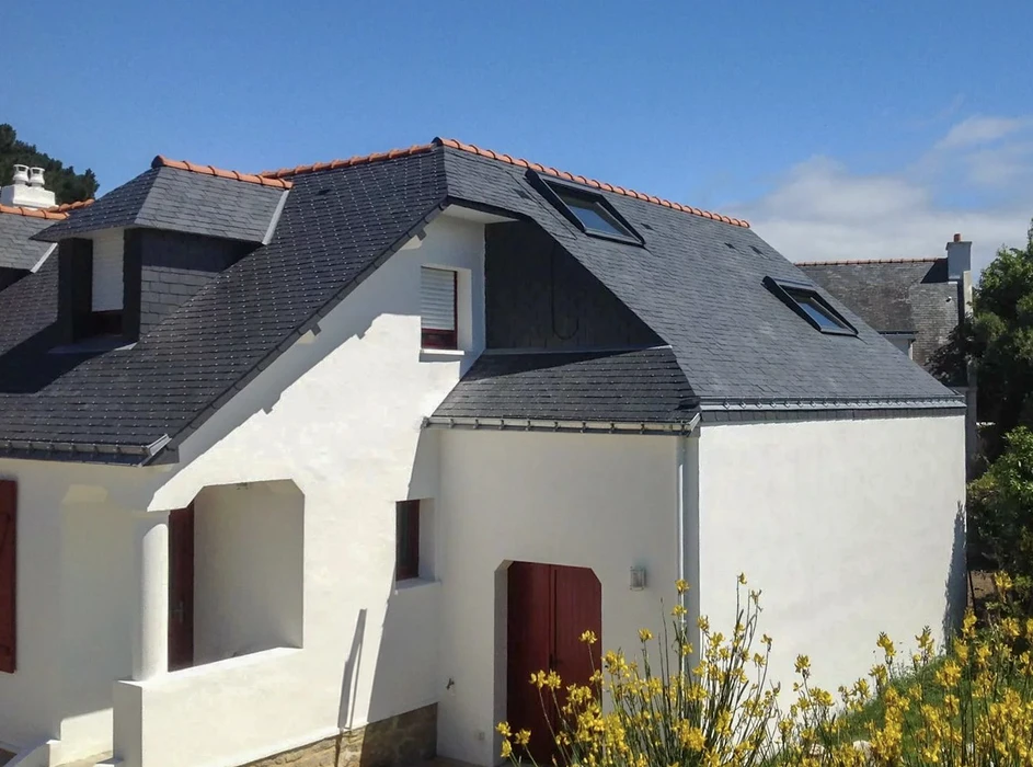 Toiture résidentielle moderne avec couverture en ardoises grises, lucarnes à volets noirs, cheminée maçonnée et fenêtres de toit