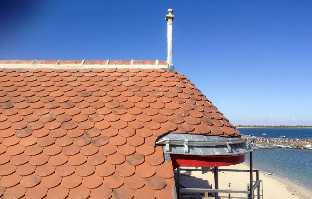 Toiture en tuiles de terre cuite sous ciel bleu dégagé, vue en contre-plongée depuis le sol