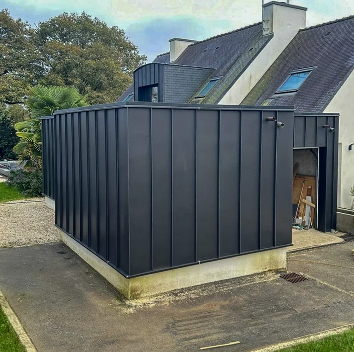 Ouvrier en équipement de sécurité haute visibilité installant une toiture métallique ondulée sur charpente industrielle au coucher du soleil