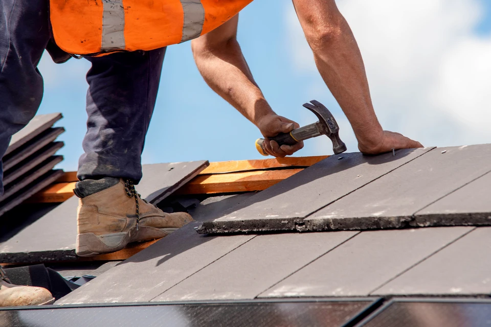 Chantier de construction extérieur avec homme en tenue de travail, casque de sécurité jaune, bras croisés devant bâtiments en construction